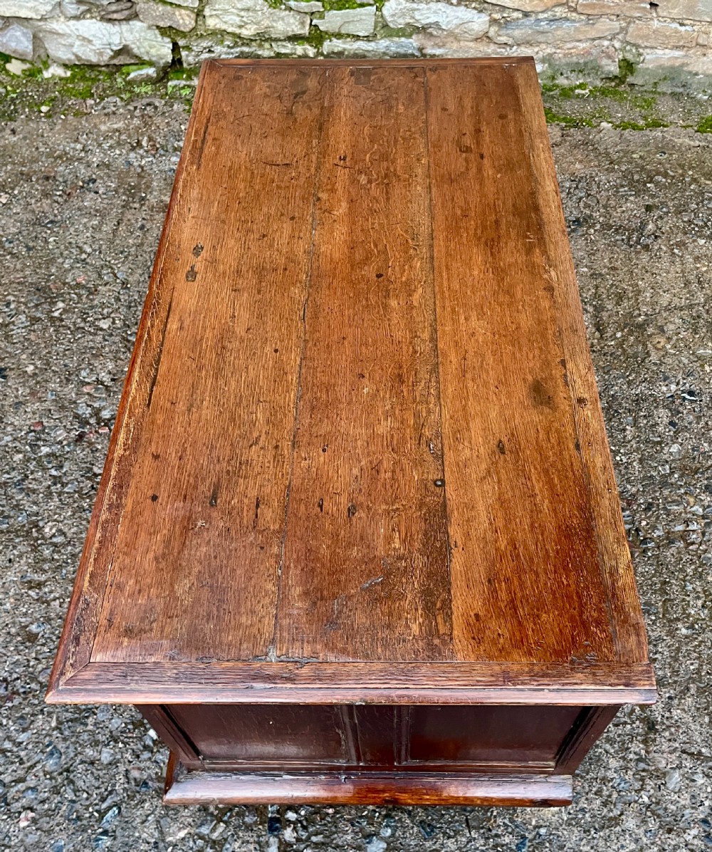 A solid oak blanket chest featuring dual fielded front panels, a central brass keyhole escutcheon, and a carved decorative apron along the base. View XIV