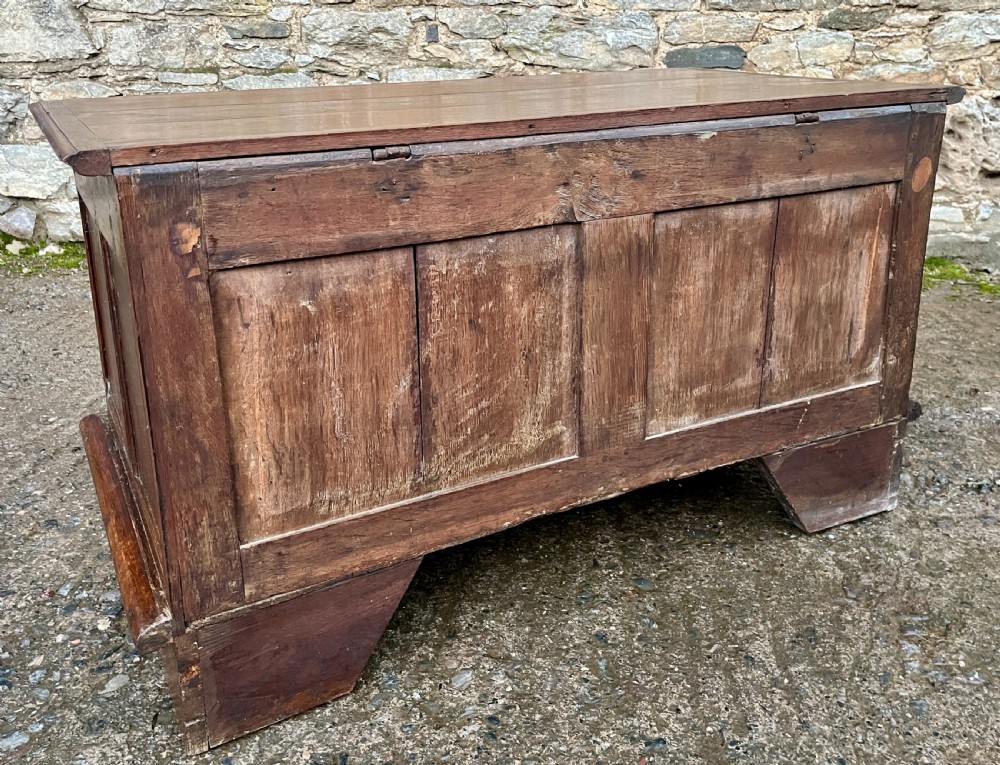 A solid oak blanket chest featuring dual fielded front panels, a central brass keyhole escutcheon, and a carved decorative apron along the base. View XVI