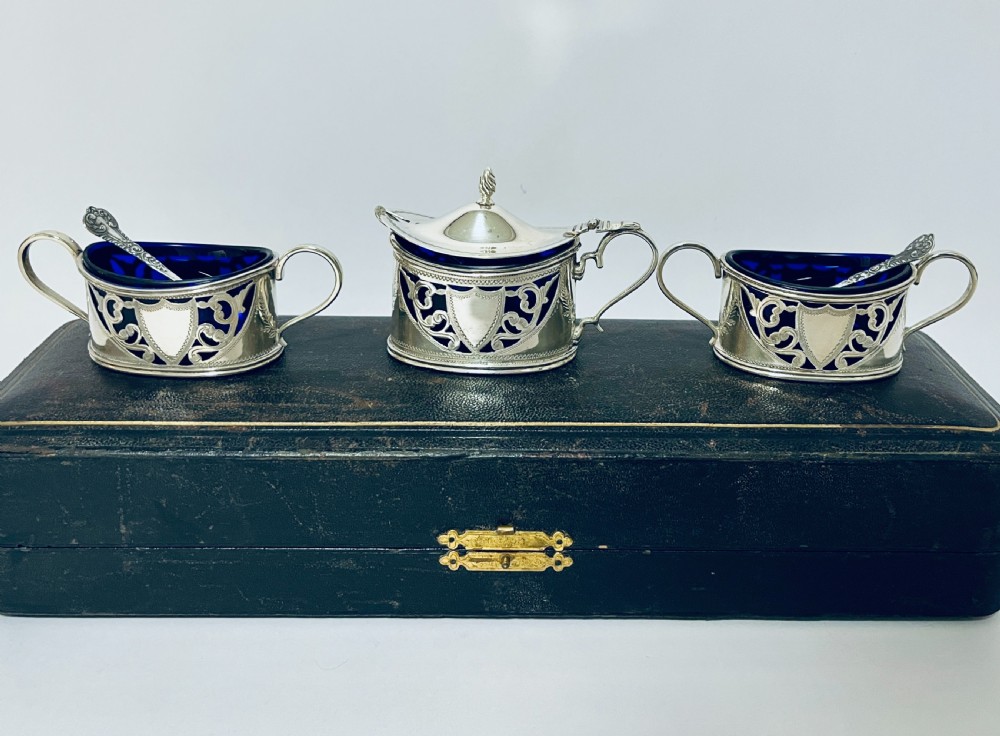 A three-piece Victorian silver condiment set with matching spoons displayed inside a fitted blue satin-lined dark presentation case. View III