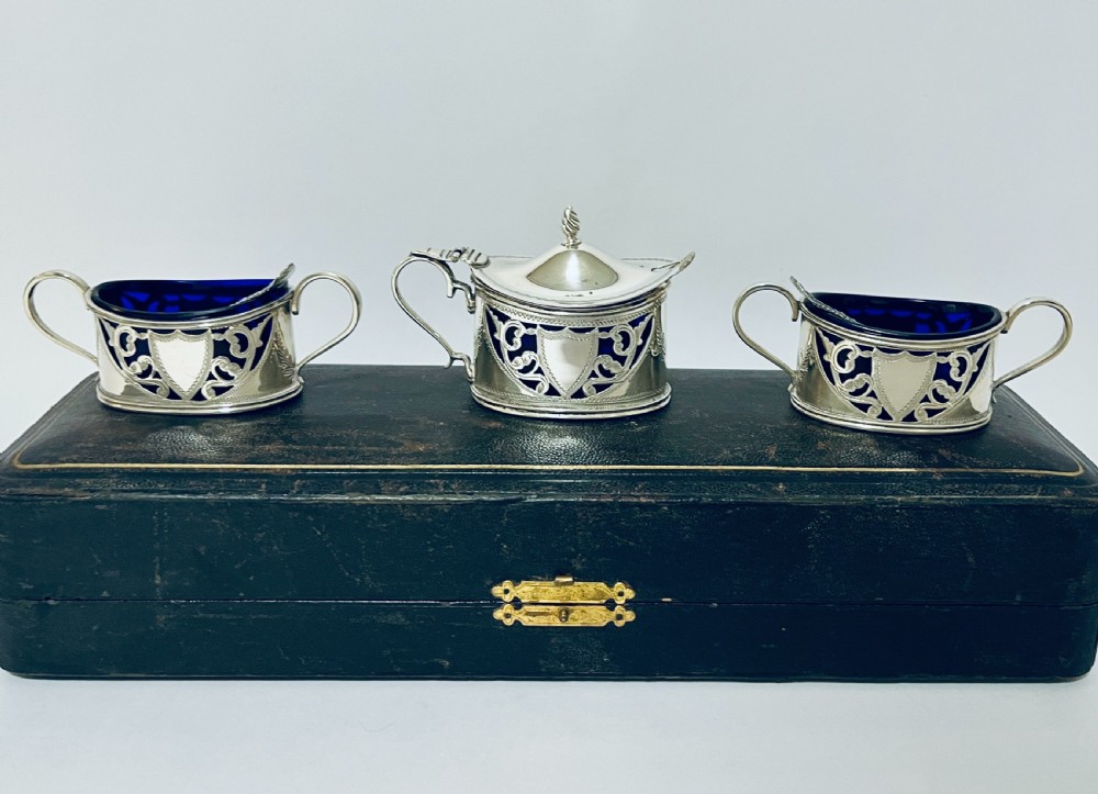 A three-piece Victorian silver condiment set with matching spoons displayed inside a fitted blue satin-lined dark presentation case. View IV