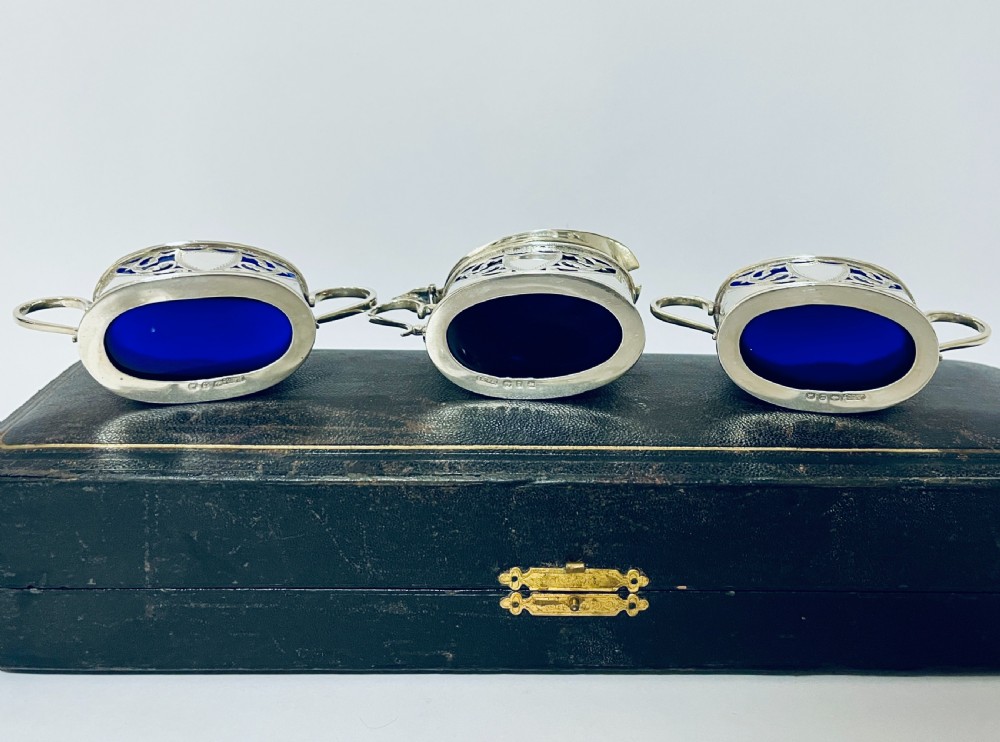 A three-piece Victorian silver condiment set with matching spoons displayed inside a fitted blue satin-lined dark presentation case. View V