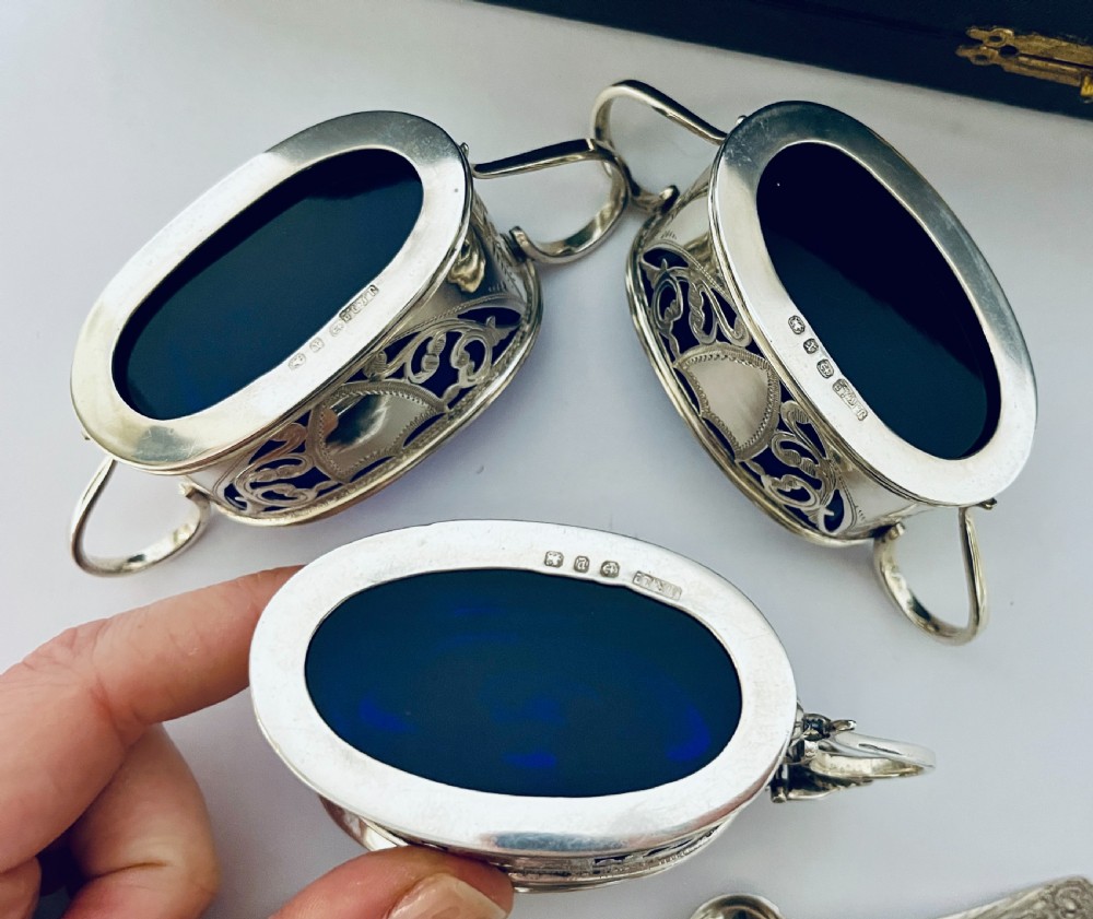 A three-piece Victorian silver condiment set with matching spoons displayed inside a fitted blue satin-lined dark presentation case. View VI