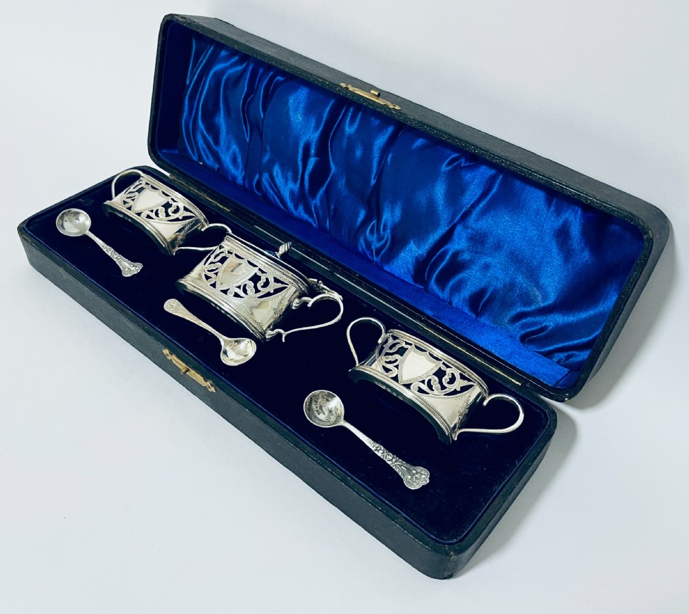 A three-piece Victorian silver condiment set with matching spoons displayed inside a fitted blue satin-lined dark presentation case. View VIII