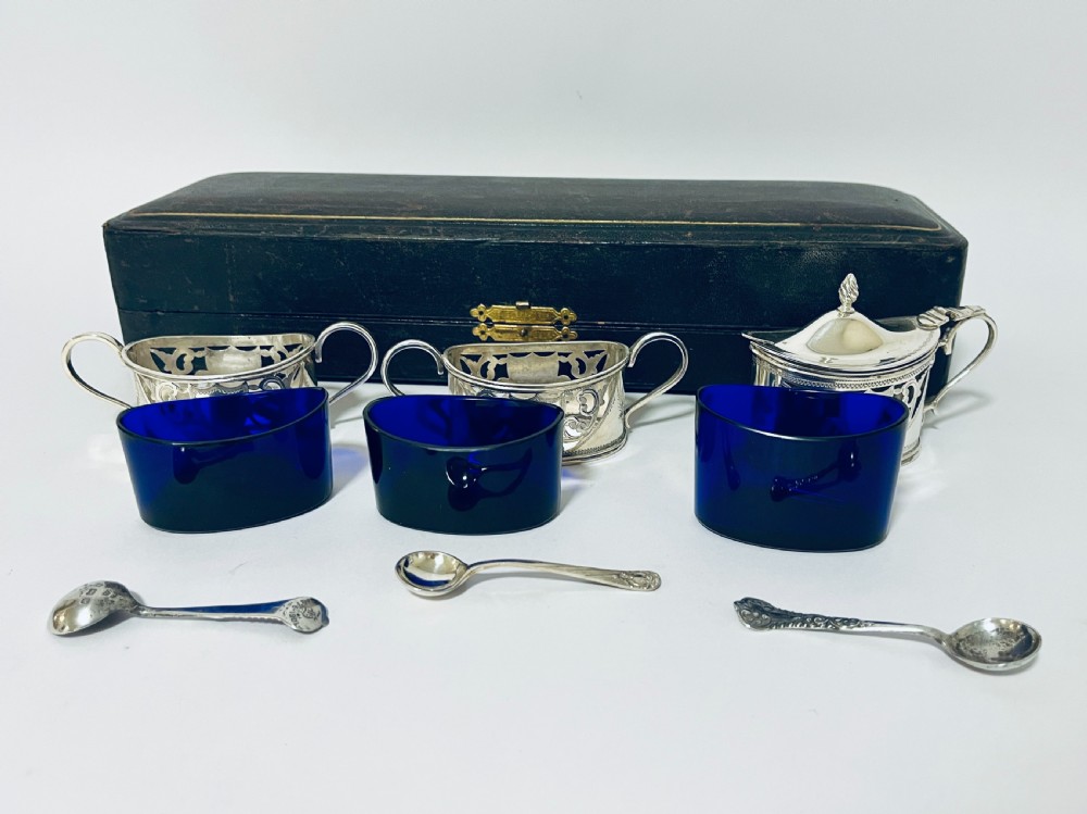 A three-piece Victorian silver condiment set with matching spoons displayed inside a fitted blue satin-lined dark presentation case. View X