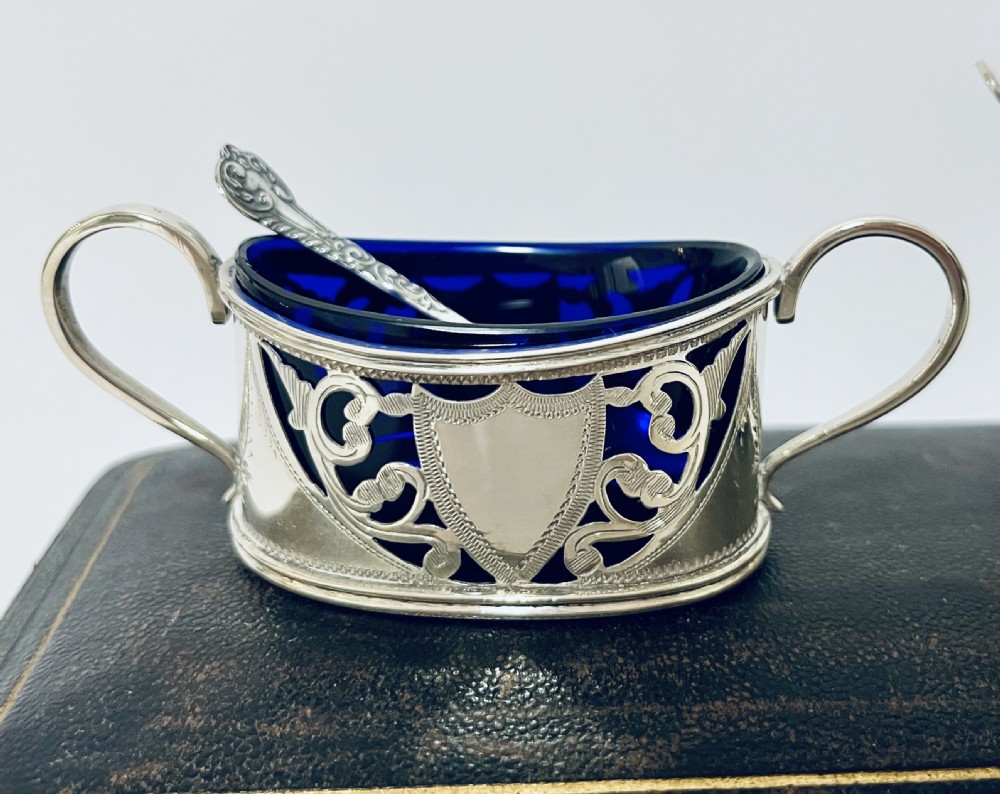 A three-piece Victorian silver condiment set with matching spoons displayed inside a fitted blue satin-lined dark presentation case. View XVI