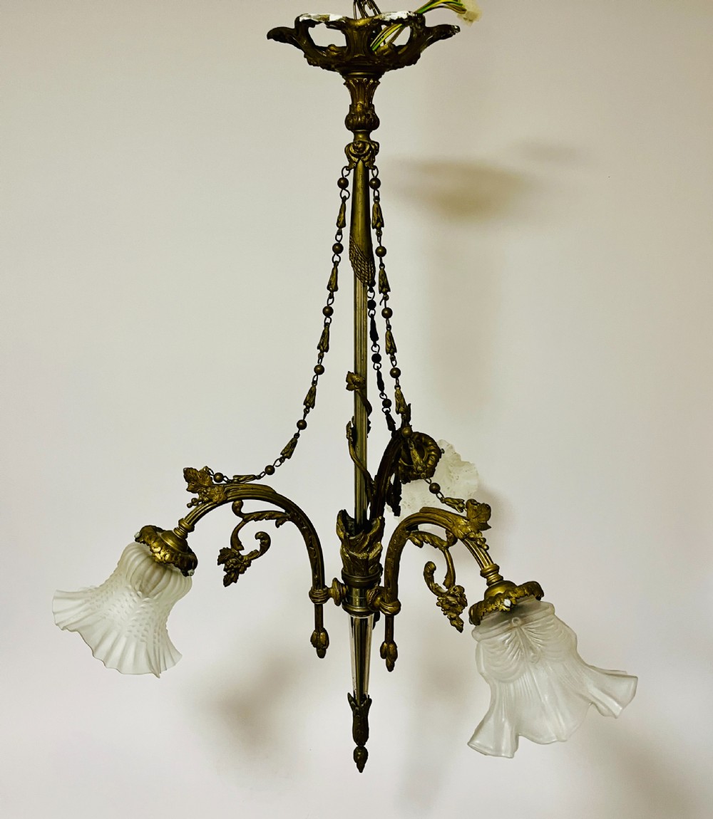 A French Empire style bronze chandelier featuring three ornate scrolling arms with frosted glass ruffled shades and hanging chain details.