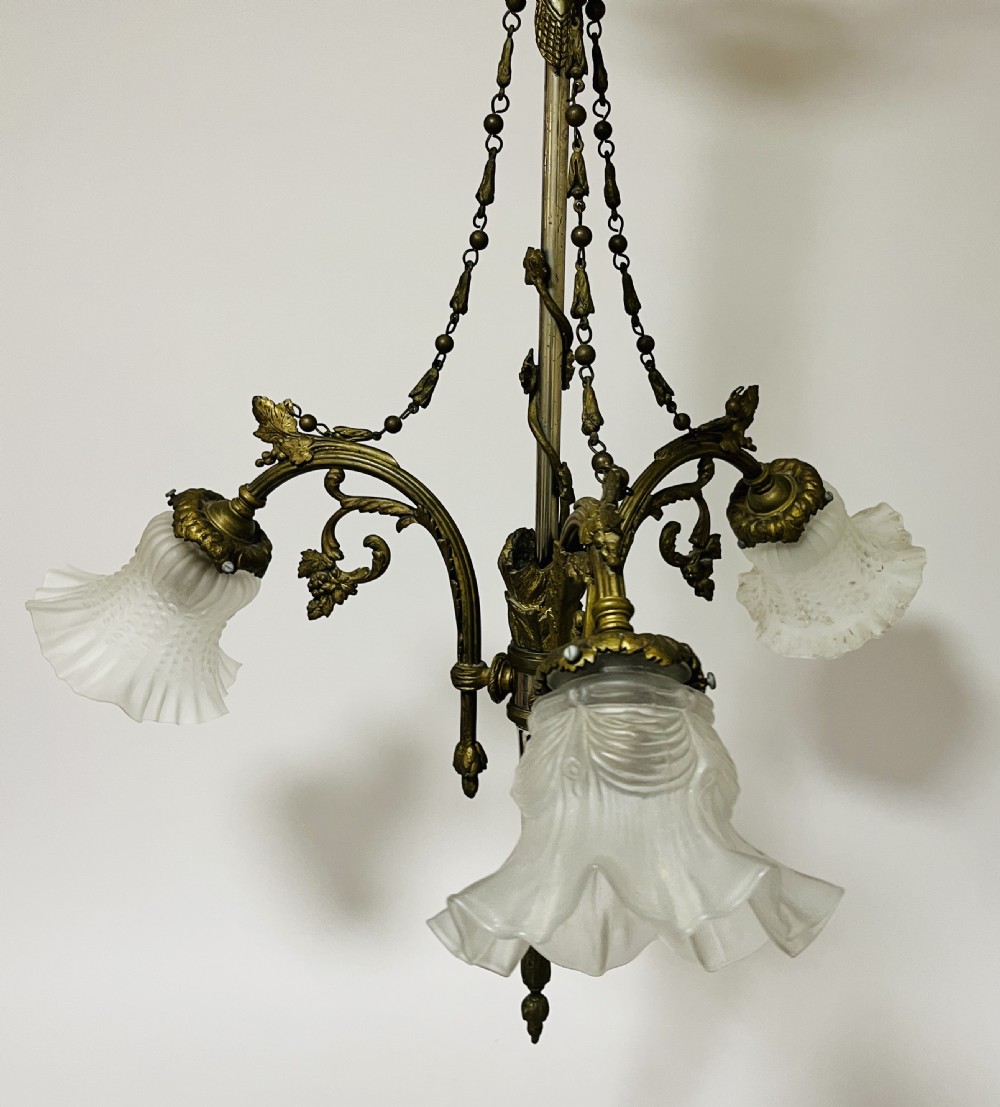 A French Empire style bronze chandelier featuring three ornate scrolling arms with frosted glass ruffled shades and hanging chain details. View II
