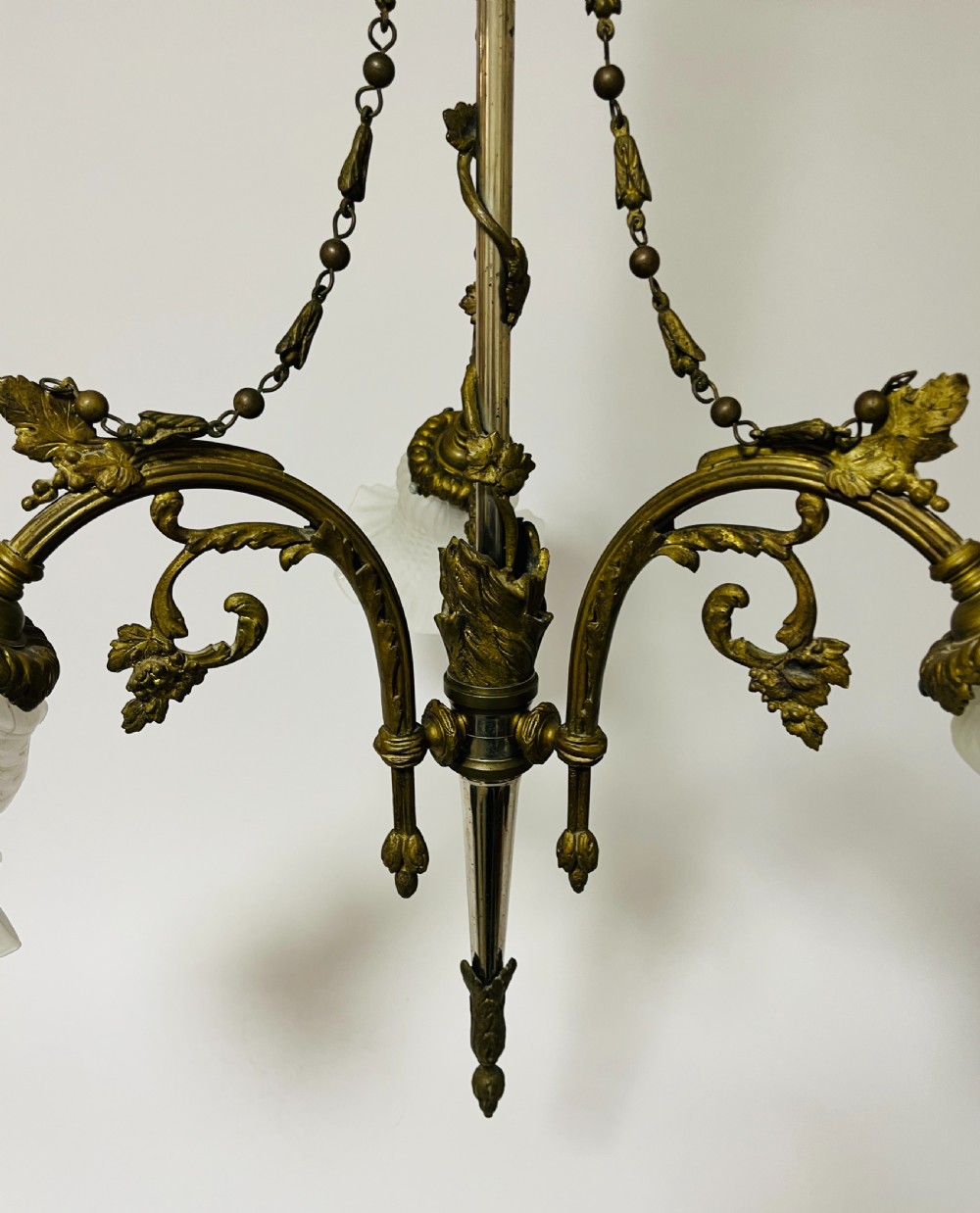 A French Empire style bronze chandelier featuring three ornate scrolling arms with frosted glass ruffled shades and hanging chain details. View V