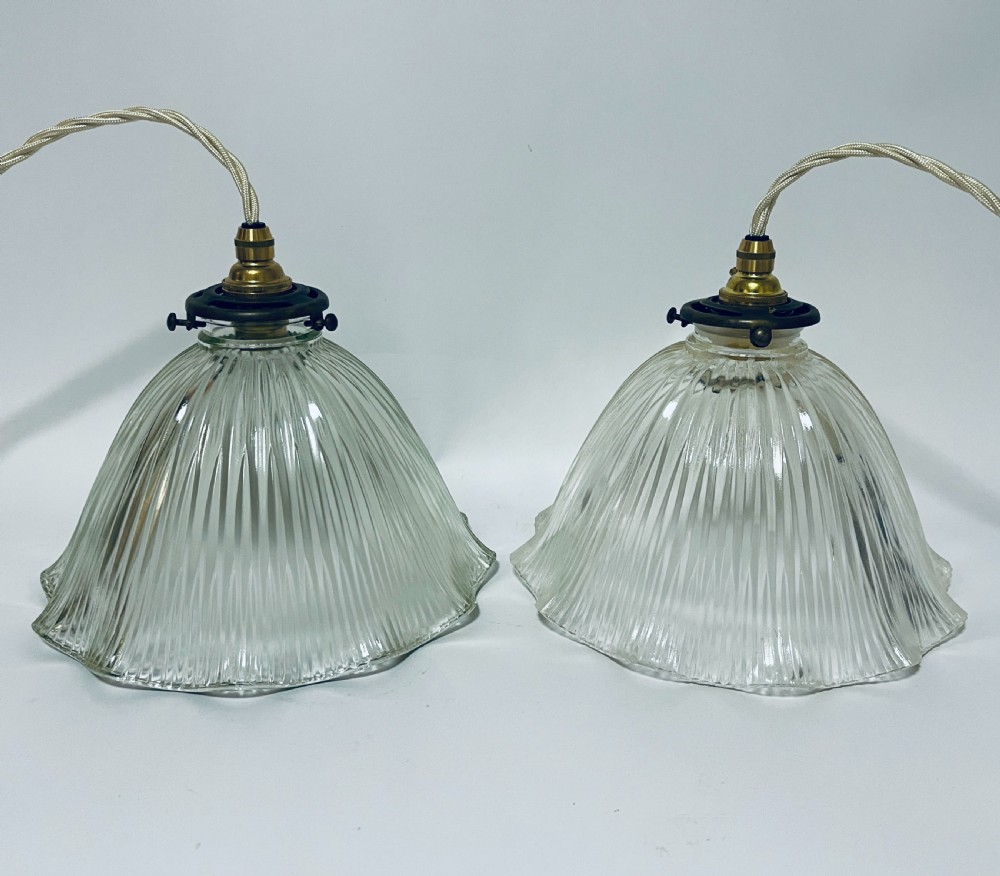 A pair of clear ribbed prismatic glass pendant light shades fitted with brass collars and light braided flex cords.