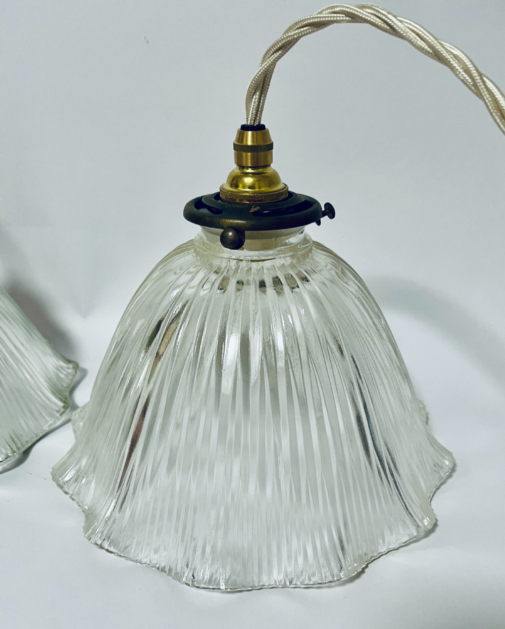 A pair of clear ribbed prismatic glass pendant light shades fitted with brass collars and light braided flex cords. View II
