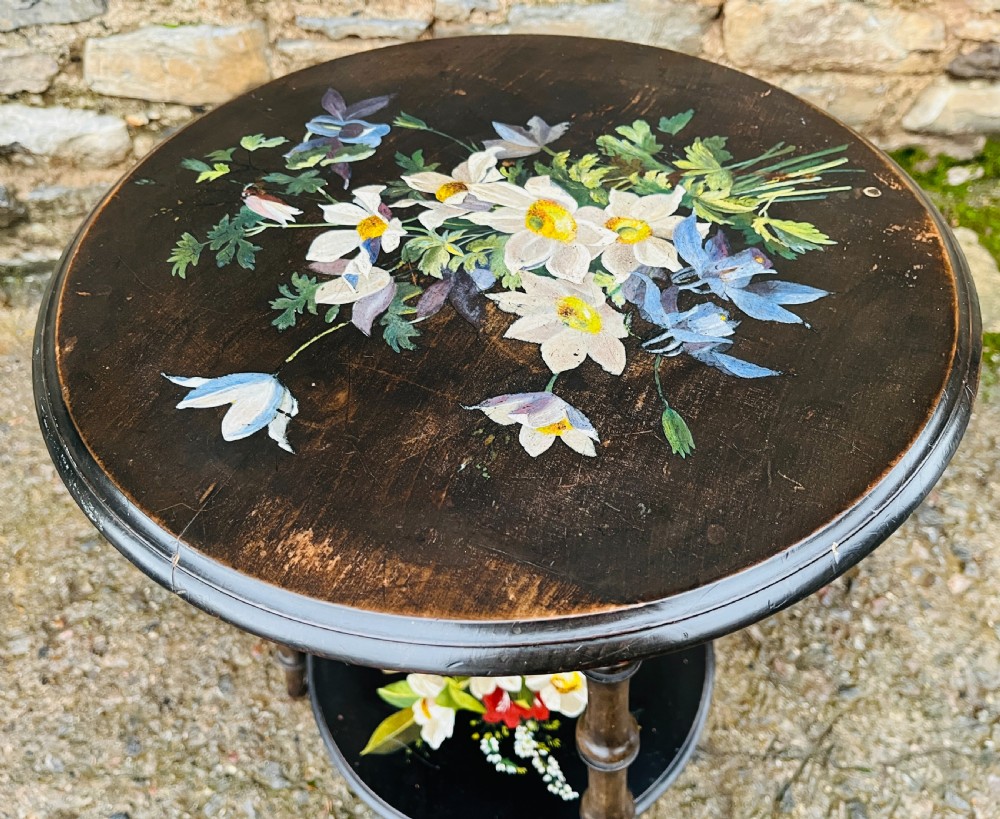 A circular two-tiered ebonised wooden side table featuring turned bobbin legs and hand-painted floral arrangements on both levels. View V