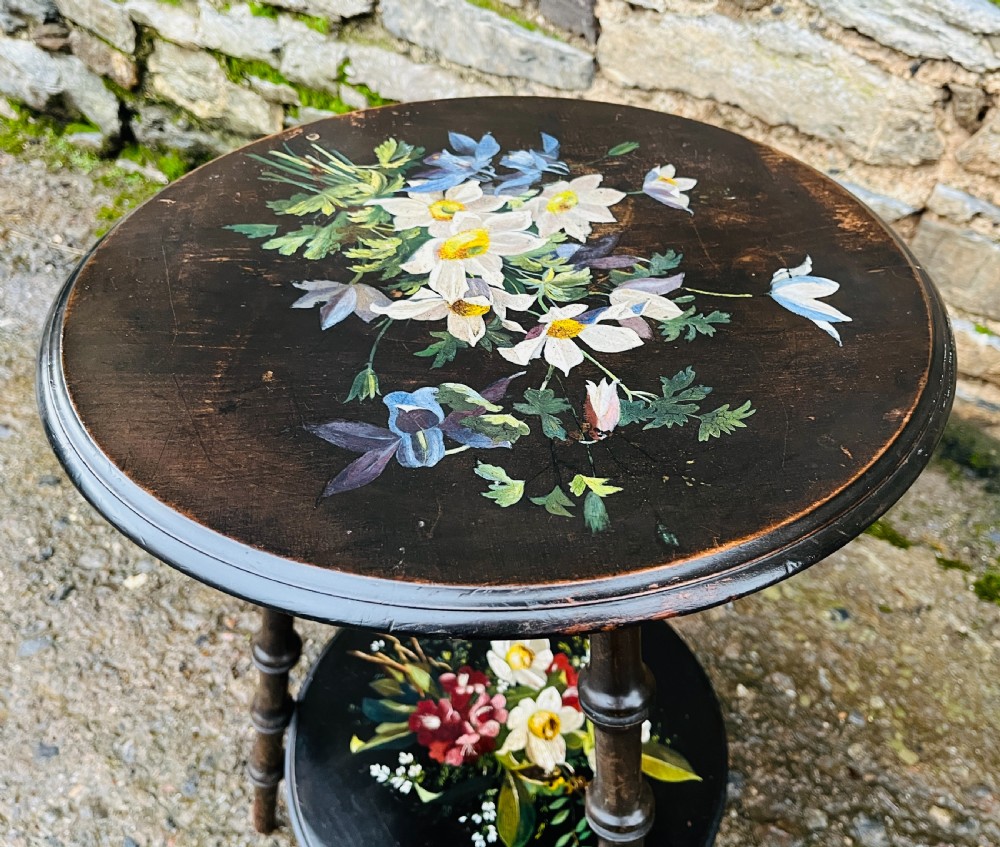 A circular two-tiered ebonised wooden side table featuring turned bobbin legs and hand-painted floral arrangements on both levels. View VIII