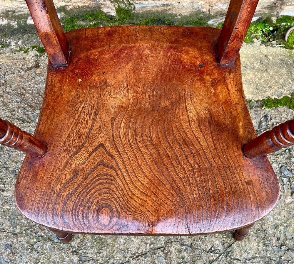 An antique wooden bar-back carver chair featuring curved armrests, turned spindle supports, a shaped seat with visible wood grain, and a warm brown finish. View III