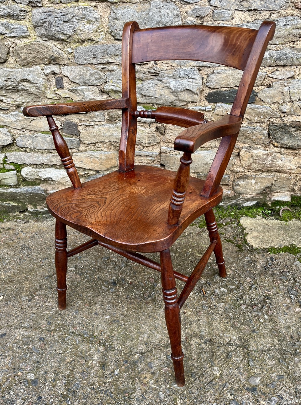 An antique wooden bar-back carver chair featuring curved armrests, turned spindle supports, a shaped seat with visible wood grain, and a warm brown finish. View IV
