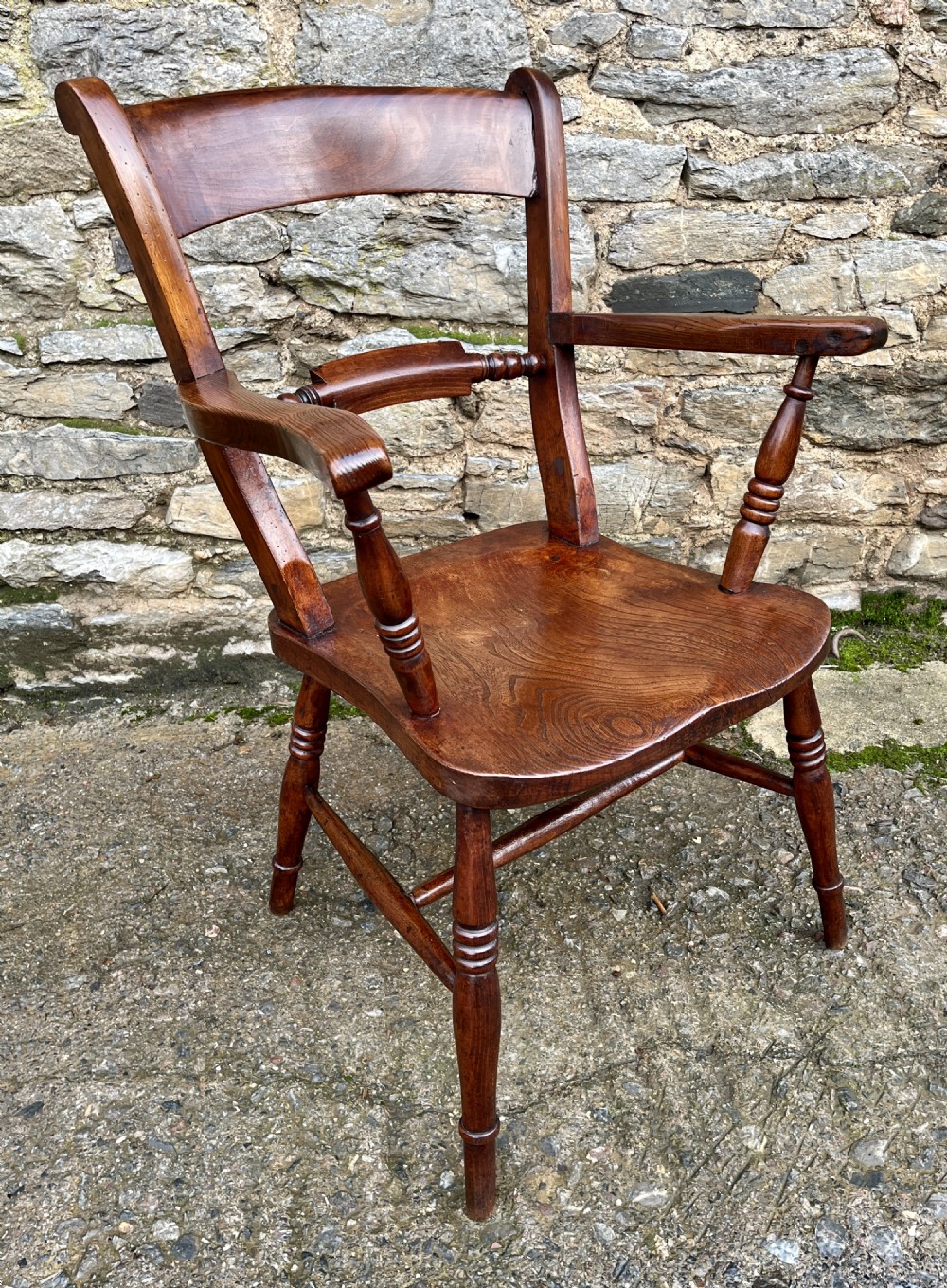 An antique wooden bar-back carver chair featuring curved armrests, turned spindle supports, a shaped seat with visible wood grain, and a warm brown finish. View IX