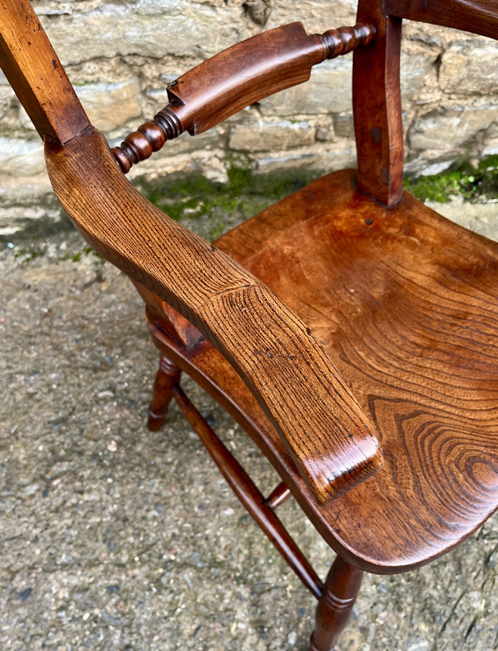 An antique wooden bar-back carver chair featuring curved armrests, turned spindle supports, a shaped seat with visible wood grain, and a warm brown finish. View XI