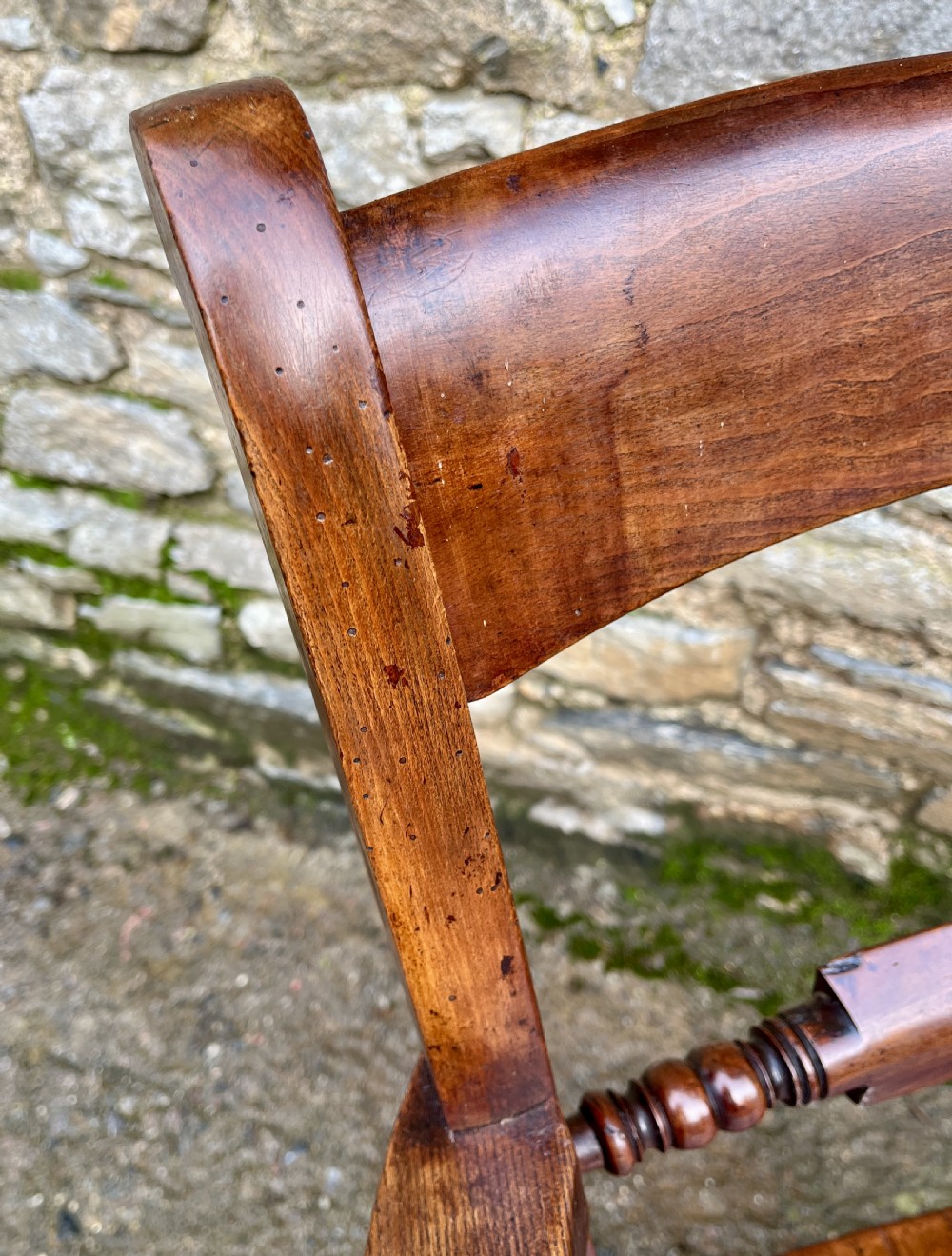 An antique wooden bar-back carver chair featuring curved armrests, turned spindle supports, a shaped seat with visible wood grain, and a warm brown finish. View XII