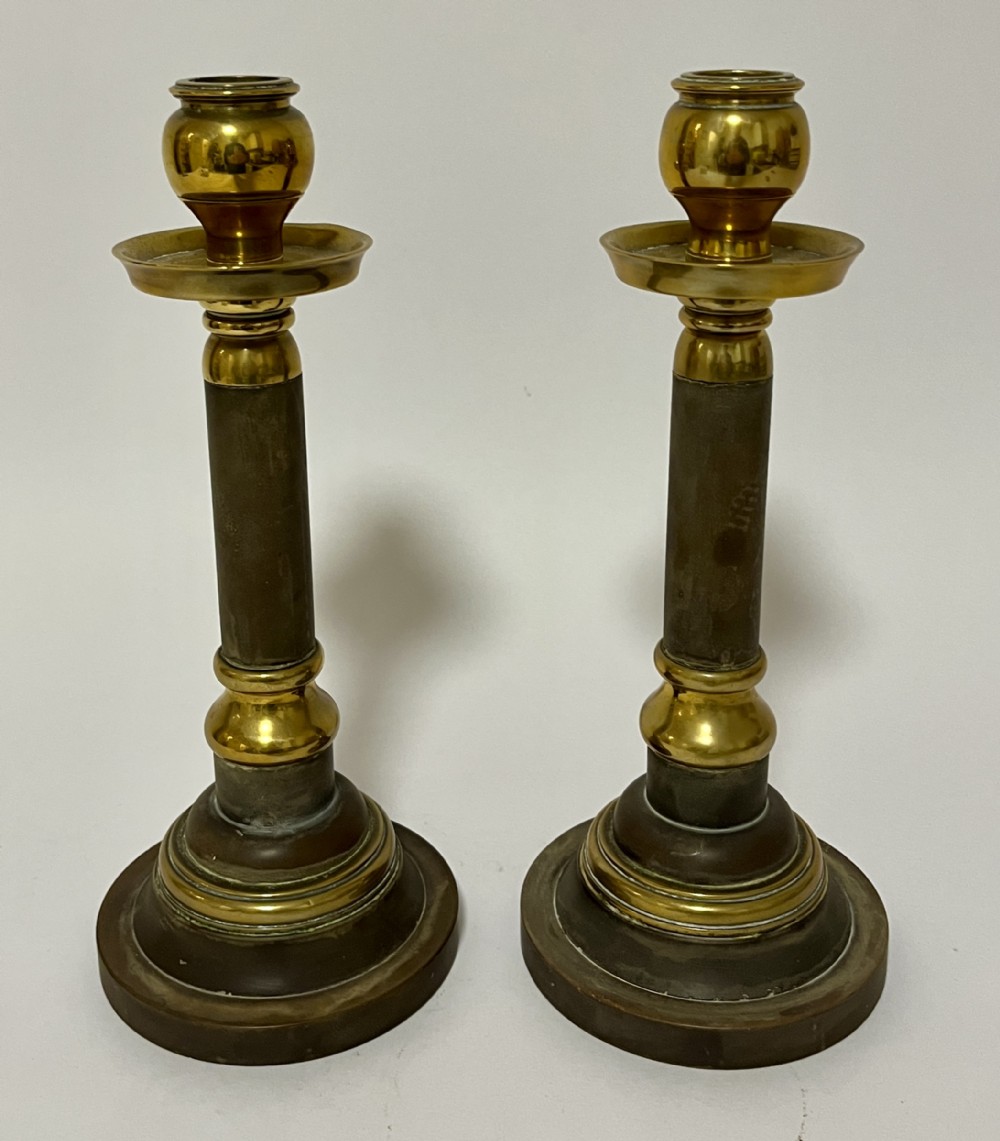 A pair of Edwardian turned brass candlesticks featuring circular stepped bases and alternating polished and patinated dark brass sections.