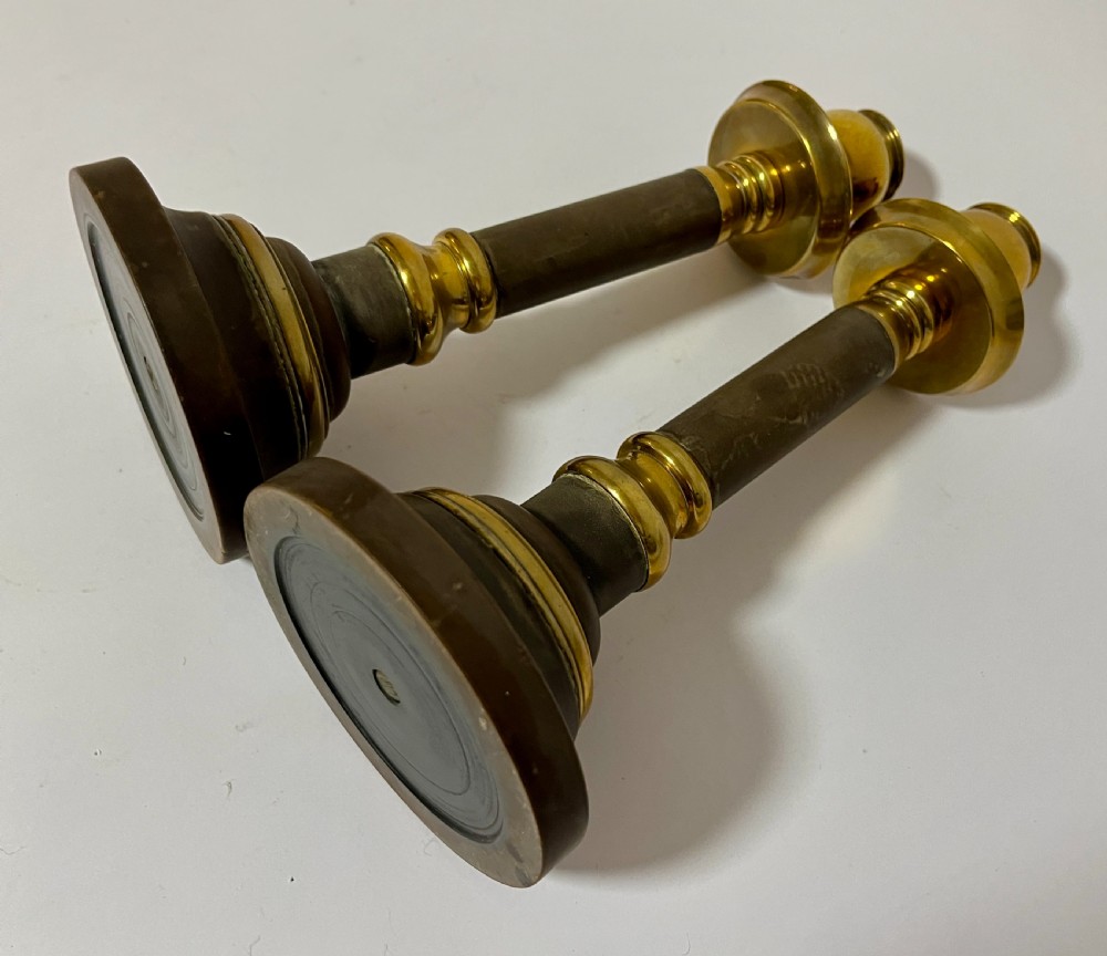 A pair of Edwardian turned brass candlesticks featuring circular stepped bases and alternating polished and patinated dark brass sections. View V