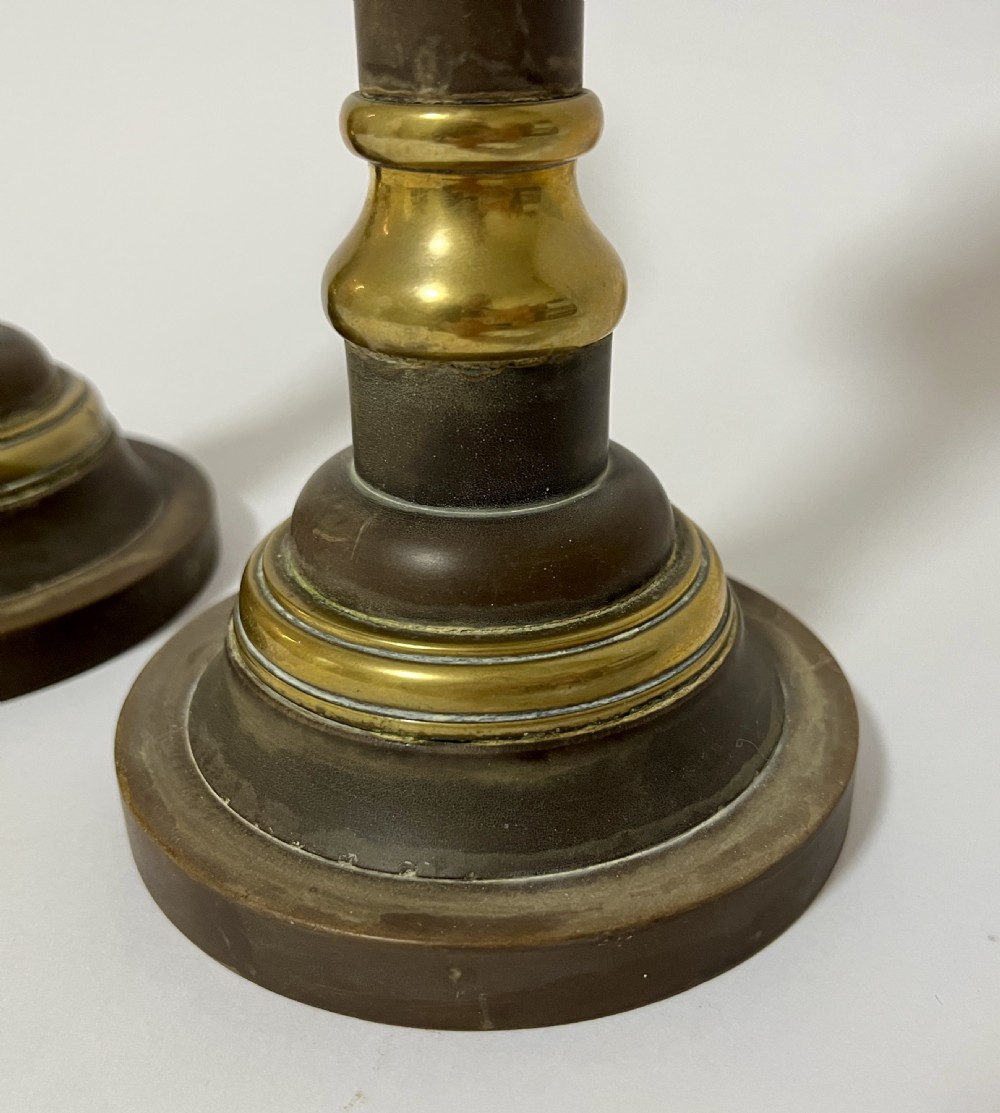A pair of Edwardian turned brass candlesticks featuring circular stepped bases and alternating polished and patinated dark brass sections. View VIII