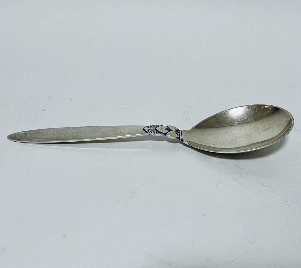 A sterling silver serving spoon in the Georg Jensen Cactus pattern featuring a smooth oval bowl and a tapered handle with stylised leaf embellishments.