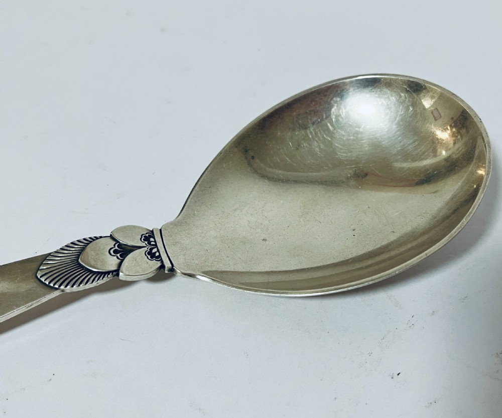 A sterling silver serving spoon in the Georg Jensen Cactus pattern featuring a smooth oval bowl and a tapered handle with stylised leaf embellishments. View III