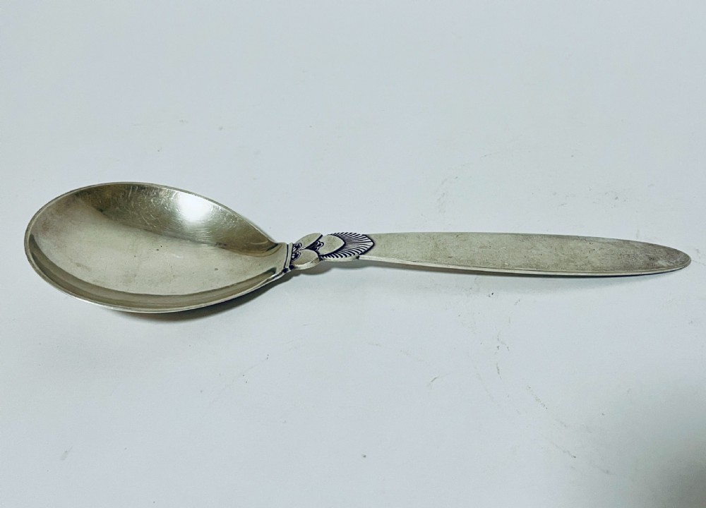 A sterling silver serving spoon in the Georg Jensen Cactus pattern featuring a smooth oval bowl and a tapered handle with stylised leaf embellishments. View V