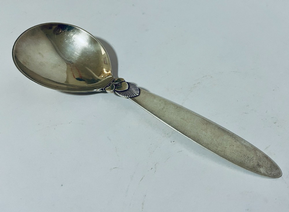 A sterling silver serving spoon in the Georg Jensen Cactus pattern featuring a smooth oval bowl and a tapered handle with stylised leaf embellishments. View VI