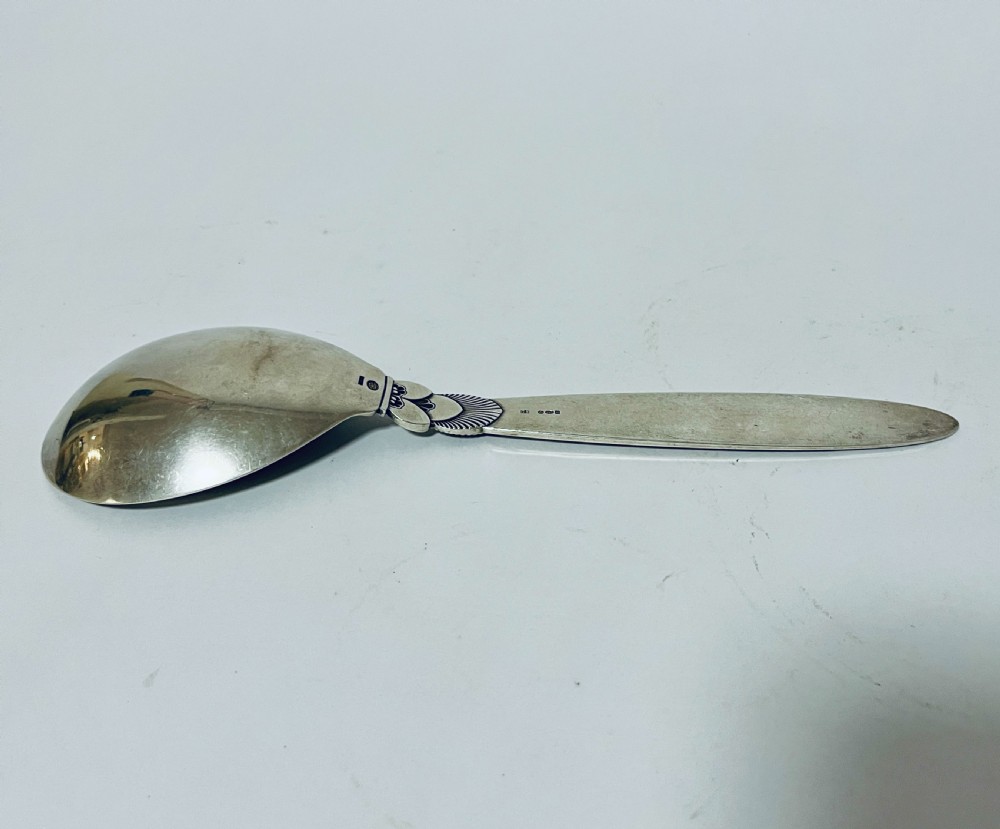 A sterling silver serving spoon in the Georg Jensen Cactus pattern featuring a smooth oval bowl and a tapered handle with stylised leaf embellishments. View VII