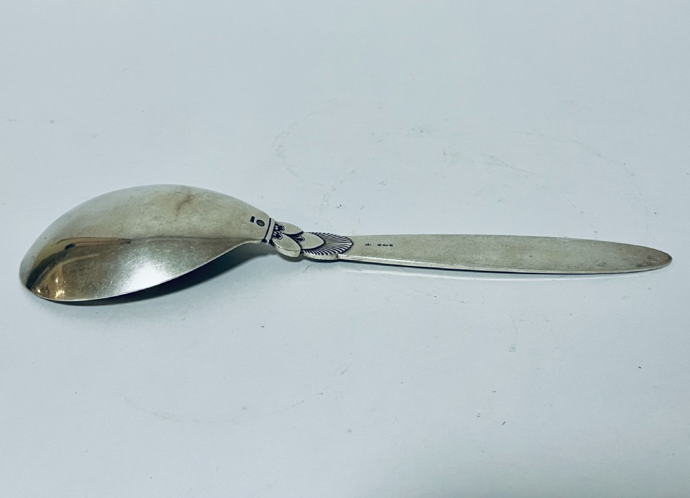 A sterling silver serving spoon in the Georg Jensen Cactus pattern featuring a smooth oval bowl and a tapered handle with stylised leaf embellishments. View XI