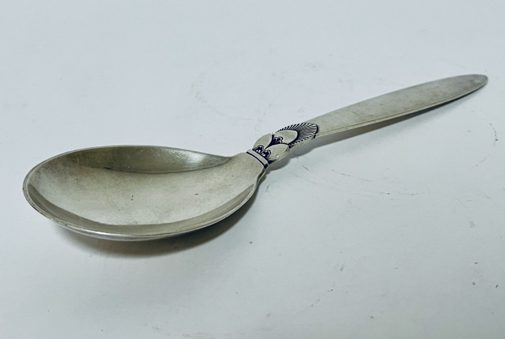 A sterling silver serving spoon in the Georg Jensen Cactus pattern featuring a smooth oval bowl and a tapered handle with stylised leaf embellishments. View XII