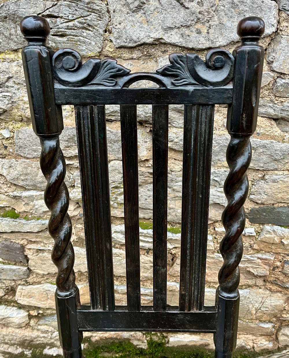 A dark 17th-century carved oak backstool with barley-twist uprights, a carved cresting rail, vertical back splats, a solid seat, and turned legs. View III