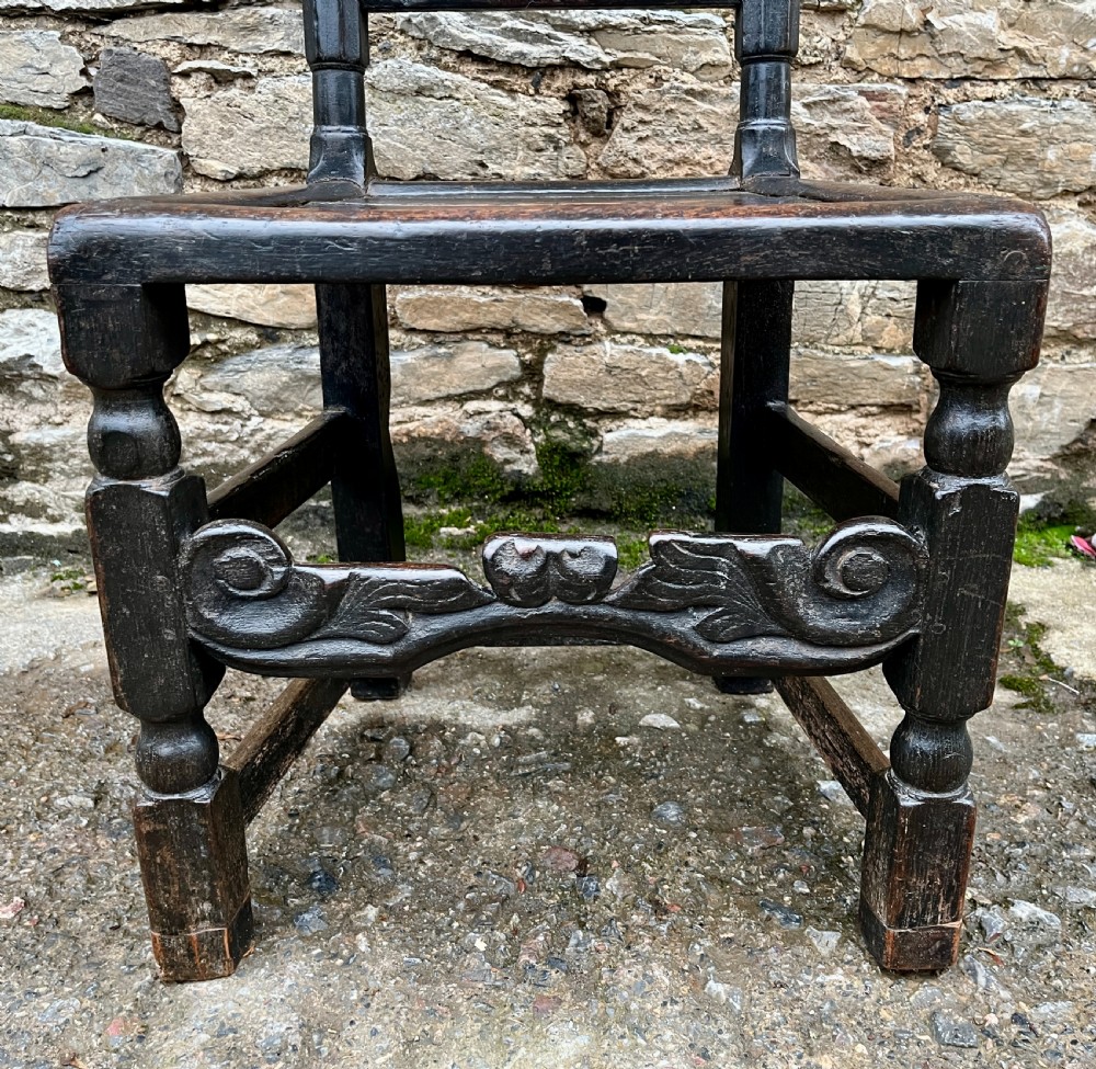 A dark 17th-century carved oak backstool with barley-twist uprights, a carved cresting rail, vertical back splats, a solid seat, and turned legs. View IV