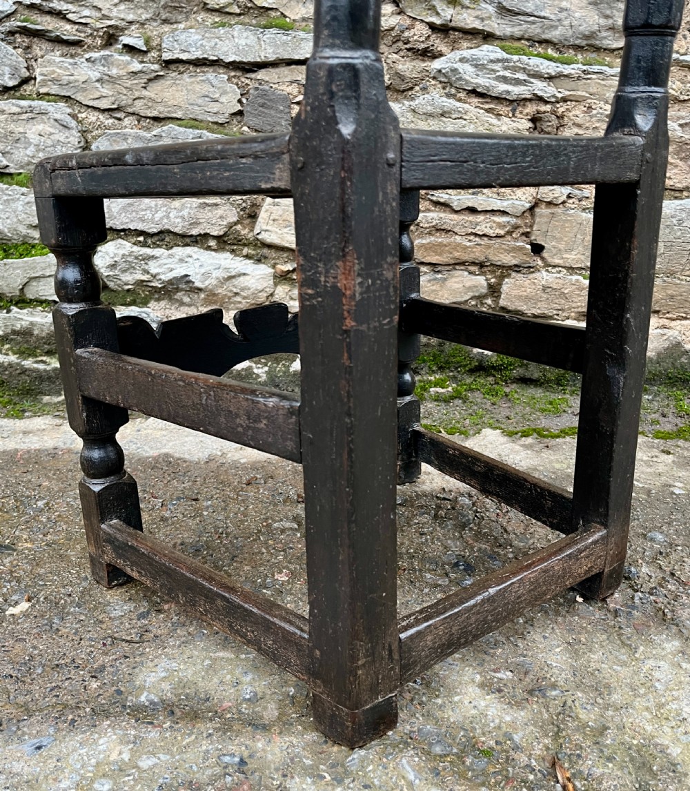 A dark 17th-century carved oak backstool with barley-twist uprights, a carved cresting rail, vertical back splats, a solid seat, and turned legs. View VIII