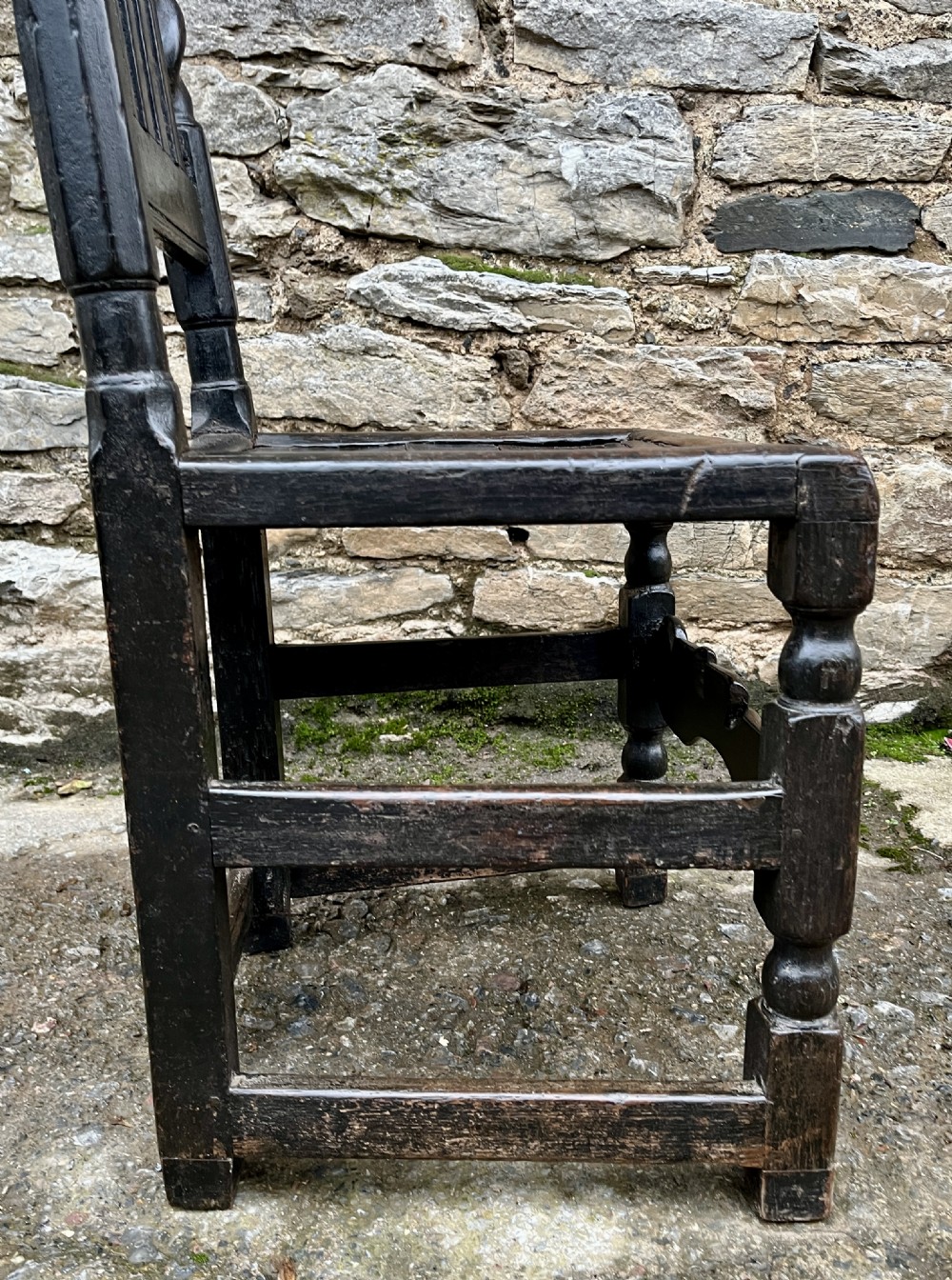 A dark 17th-century carved oak backstool with barley-twist uprights, a carved cresting rail, vertical back splats, a solid seat, and turned legs. View X