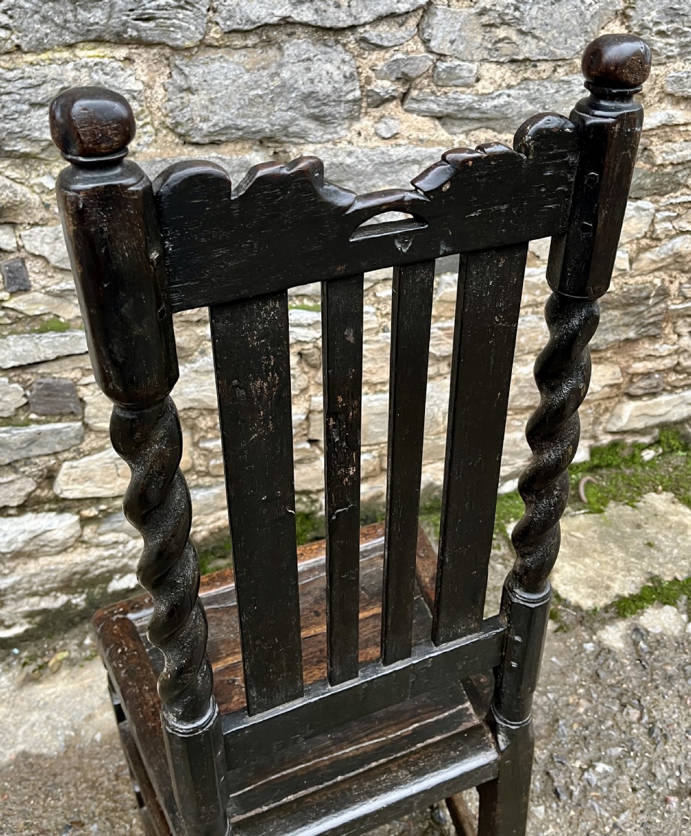 A dark 17th-century carved oak backstool with barley-twist uprights, a carved cresting rail, vertical back splats, a solid seat, and turned legs. View XI