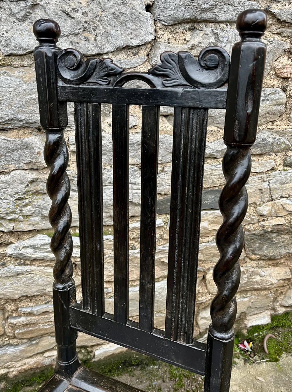 A dark 17th-century carved oak backstool with barley-twist uprights, a carved cresting rail, vertical back splats, a solid seat, and turned legs. View XIII