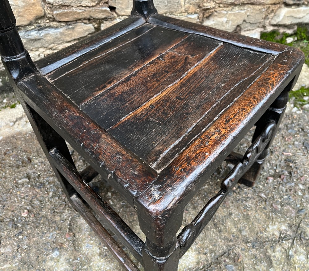 A dark 17th-century carved oak backstool with barley-twist uprights, a carved cresting rail, vertical back splats, a solid seat, and turned legs. View XVIII