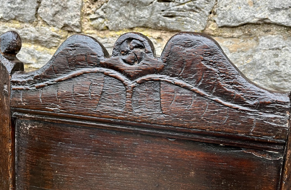 A dark oak 17th-century backstool featuring a carved crested top rail, solid wooden seat, turned front legs, and a stretchered base. View VIII