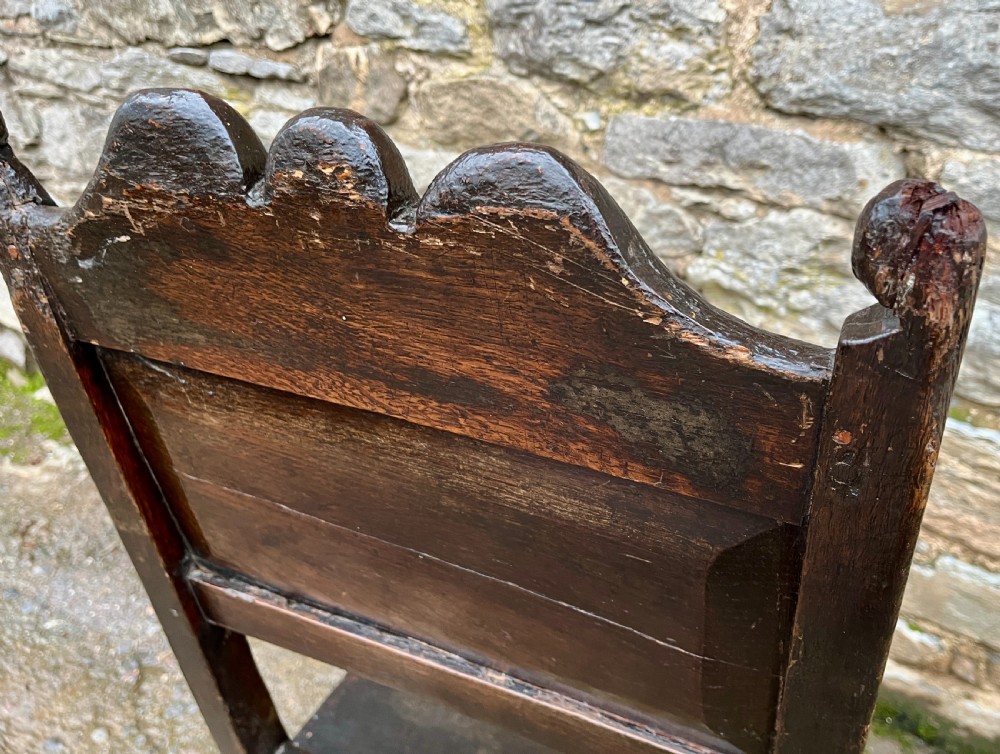 A dark oak 17th-century backstool featuring a carved crested top rail, solid wooden seat, turned front legs, and a stretchered base. View XIII