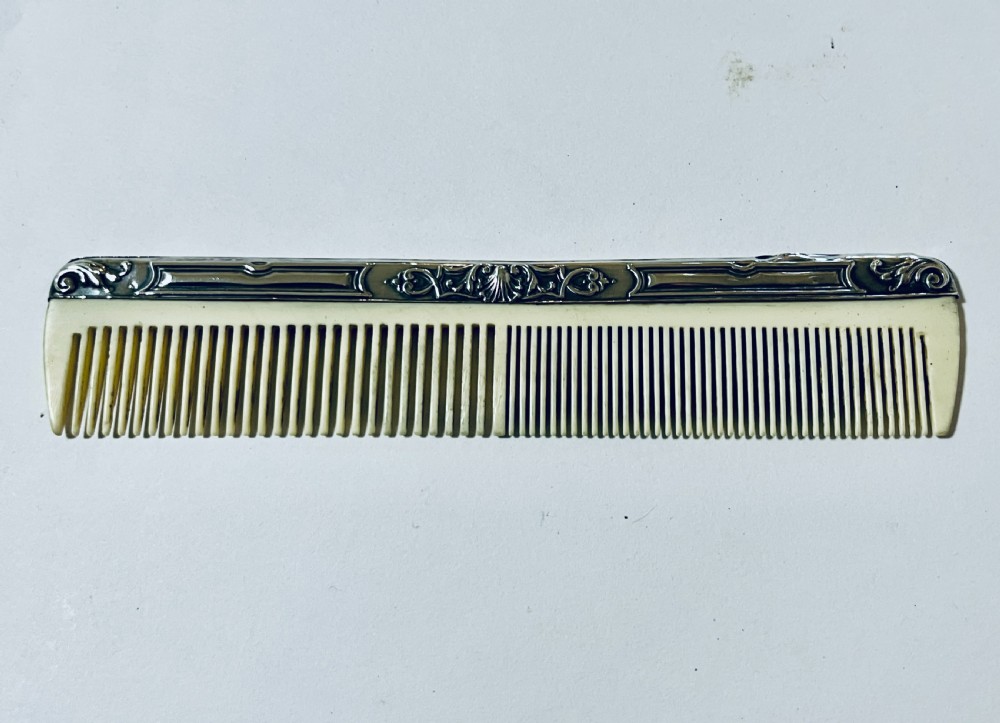 An open green textured box containing a French silver vanity set with a silver hairbrush, comb, and round lidded jar set into a yellow silk lining. View X