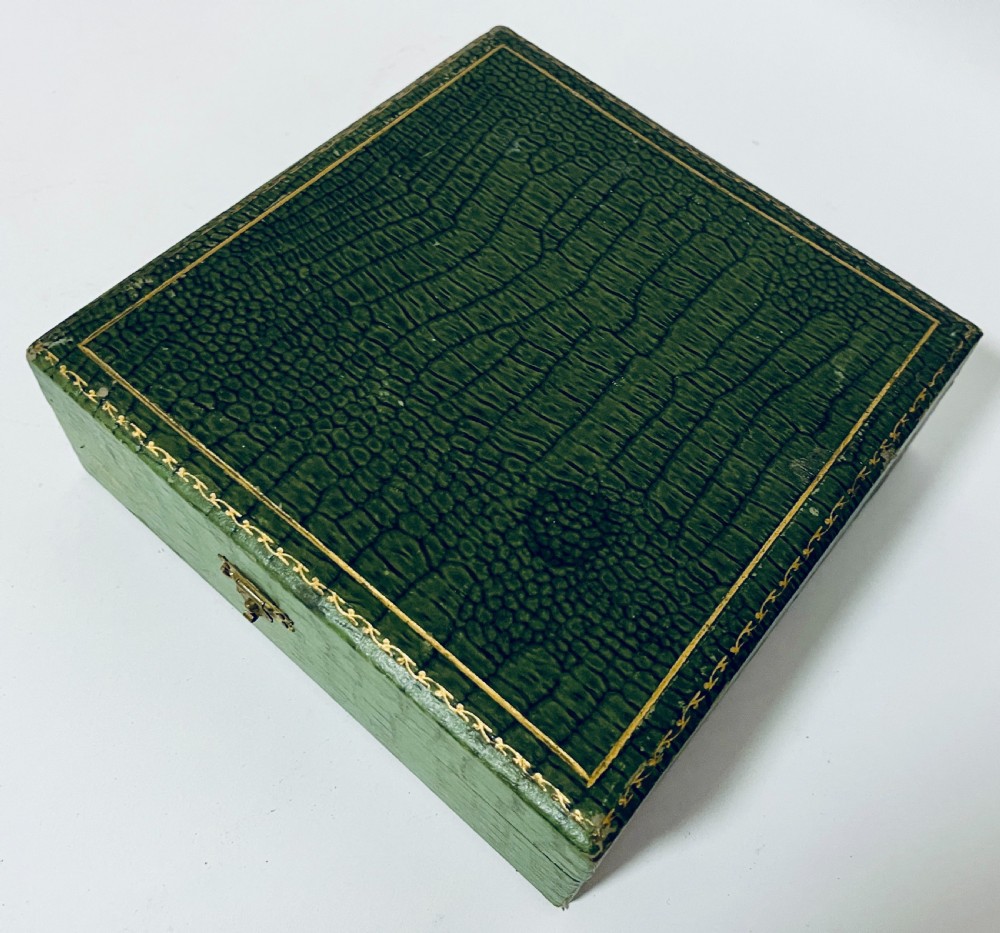 An open green textured box containing a French silver vanity set with a silver hairbrush, comb, and round lidded jar set into a yellow silk lining. View XVI