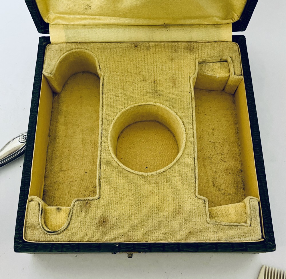 An open green textured box containing a French silver vanity set with a silver hairbrush, comb, and round lidded jar set into a yellow silk lining. View XVIII
