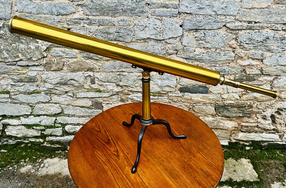 A Victorian brass library telescope supported by a black cast iron tripod desktop base.