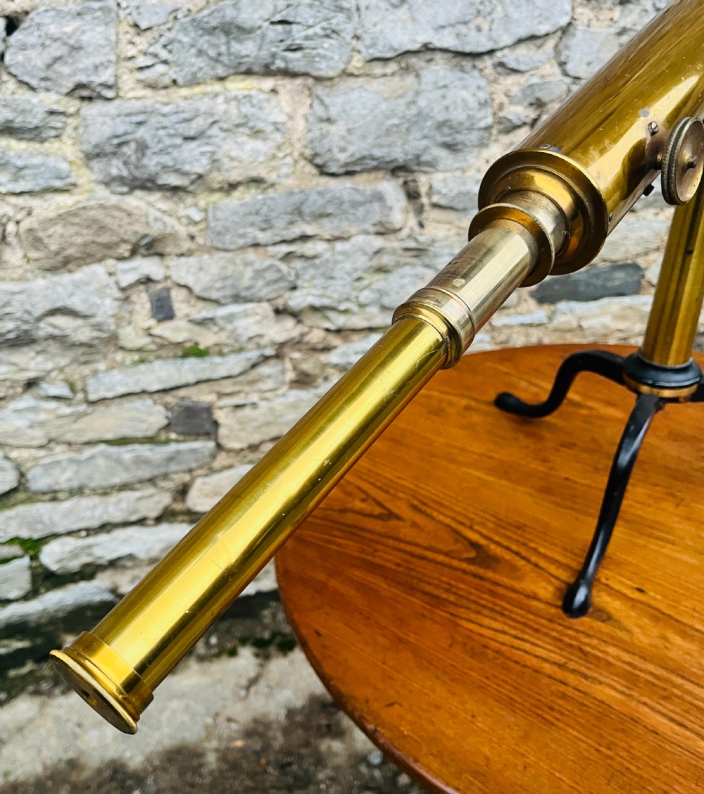 A Victorian brass library telescope supported by a black cast iron tripod desktop base. View X