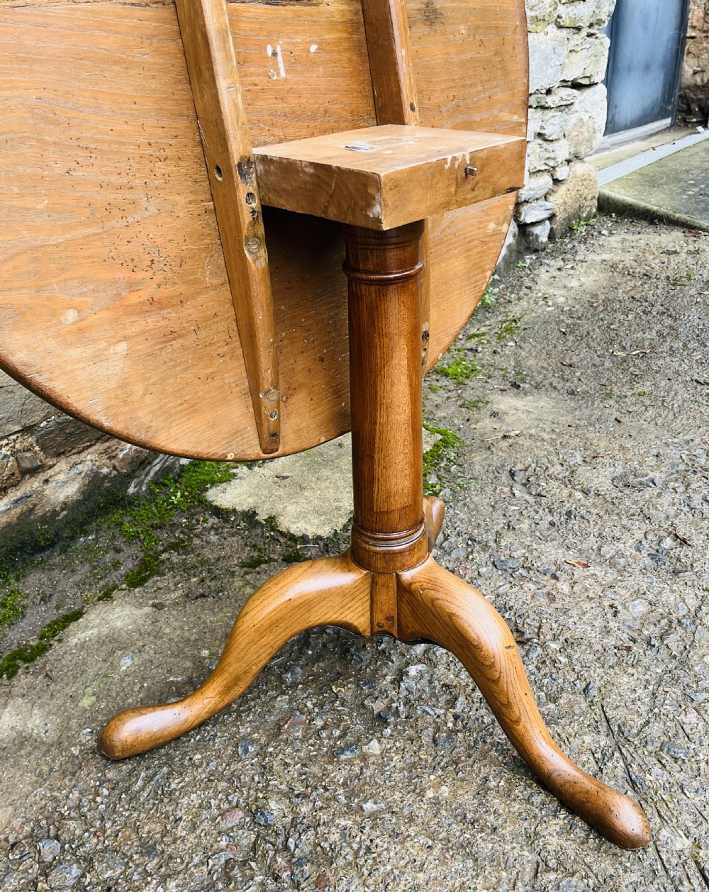 A circular Georgian oak tilt-top table resting on a central turned pedestal with three sweeping tripod legs. View X