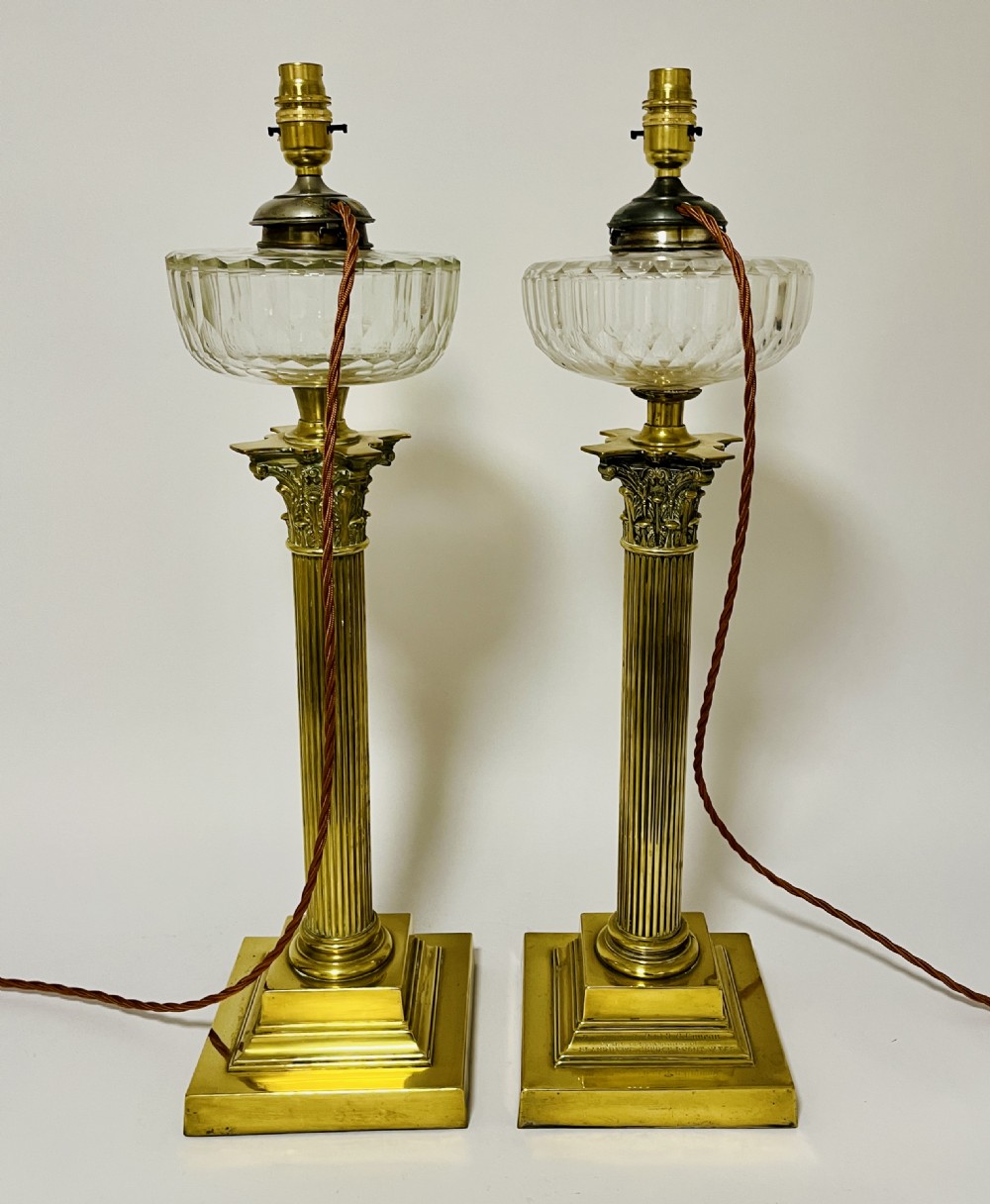 A pair of brass Corinthian column table lamps featuring stepped square plinths, fluted columns, acanthus capitals, and cut glass reservoirs. View XI