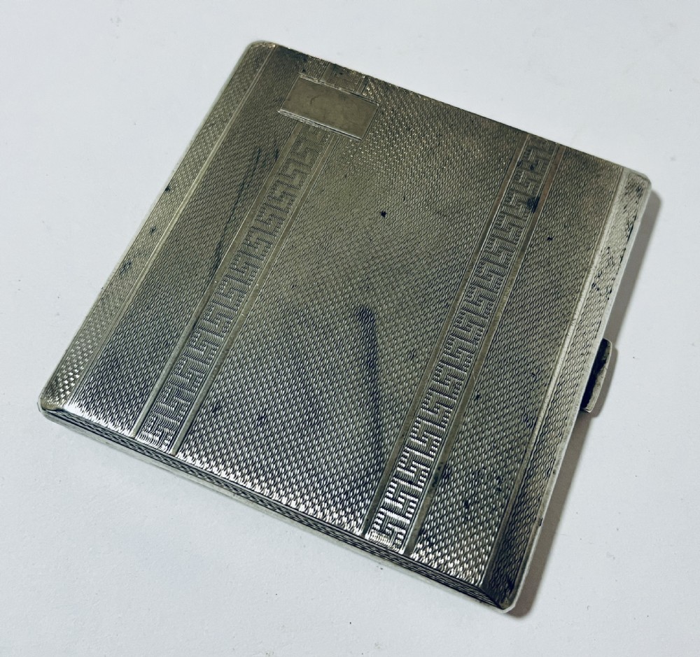 An Art Deco silver rectangular cigarette case featuring engine-turned geometric patterning and a small rectangular vacant cartouche.