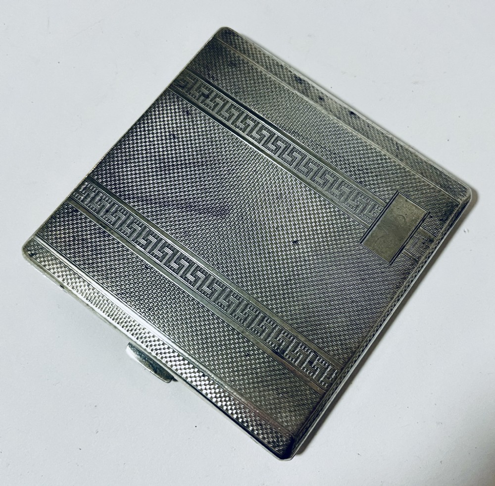 An Art Deco silver rectangular cigarette case featuring engine-turned geometric patterning and a small rectangular vacant cartouche. View IX