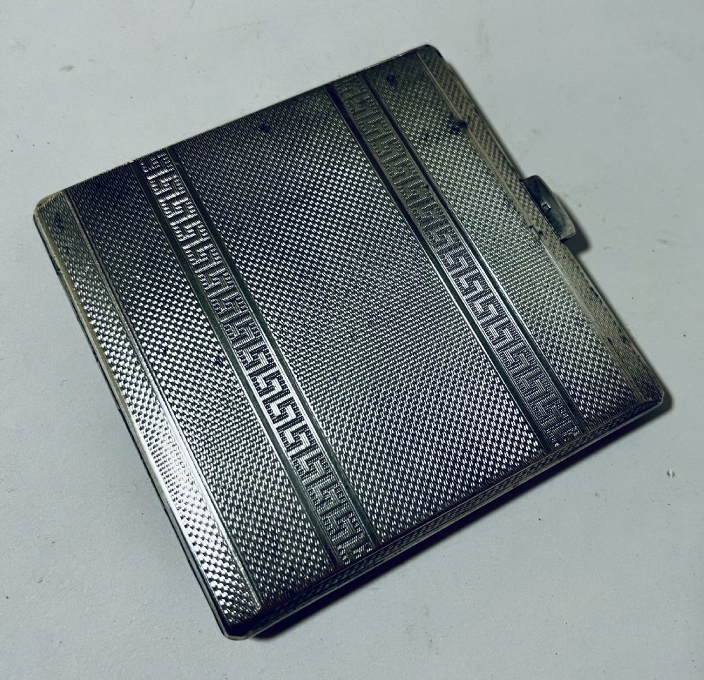 An Art Deco silver rectangular cigarette case featuring engine-turned geometric patterning and a small rectangular vacant cartouche. View XI